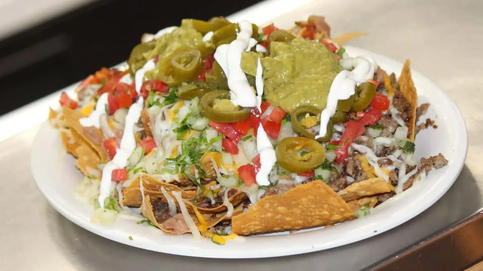 Super Nachos - A towering platter of crispy tortilla chips loaded with melted cheese, seasoned meat, jalapeños, sour cream, and fresh guacamole