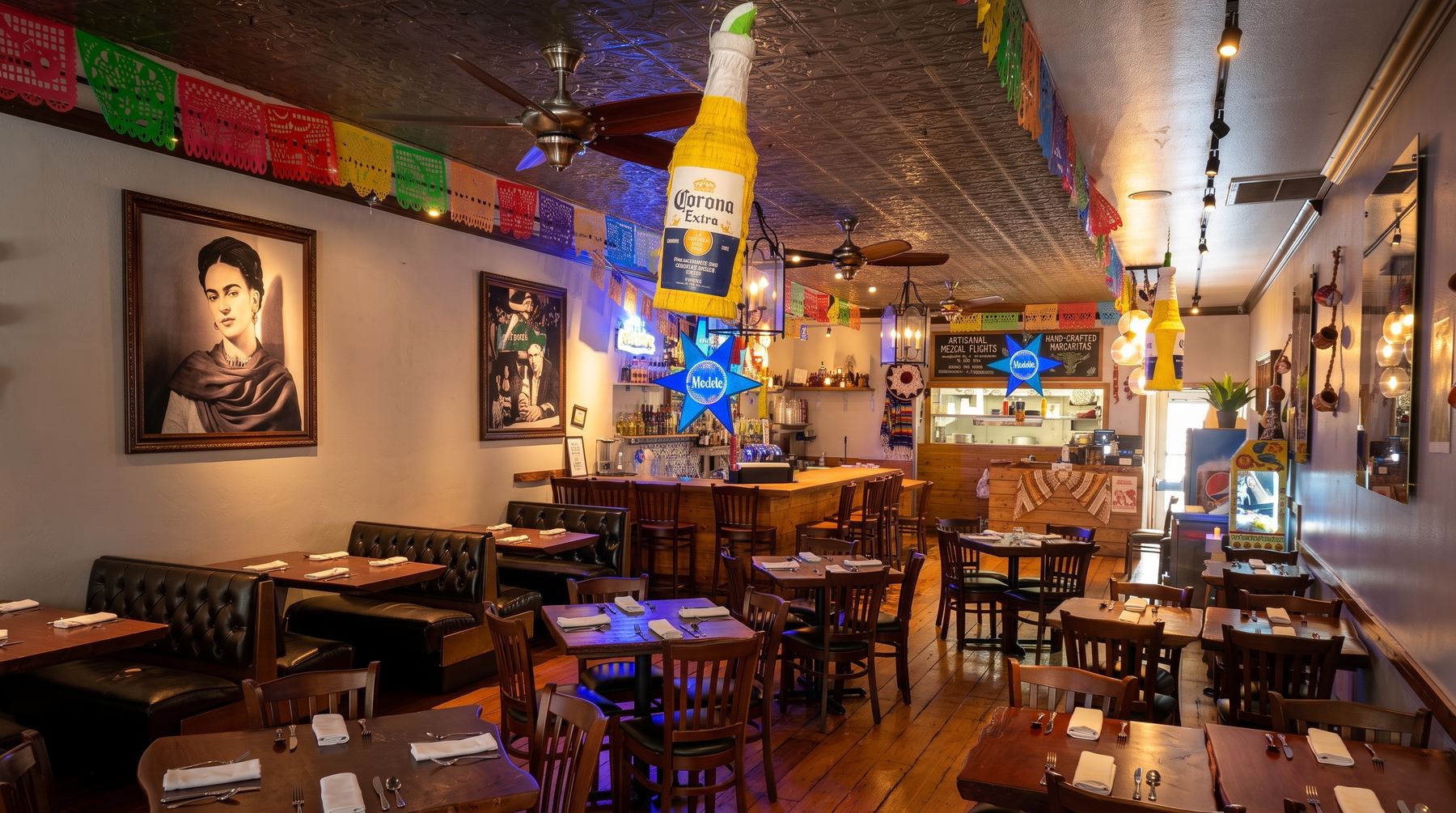 El comedor de Mi Pueblo en la calle 4th, centro de Santa Rosa: bancas de madera, papel picado bajo el techo de lámina y la barra al fondo