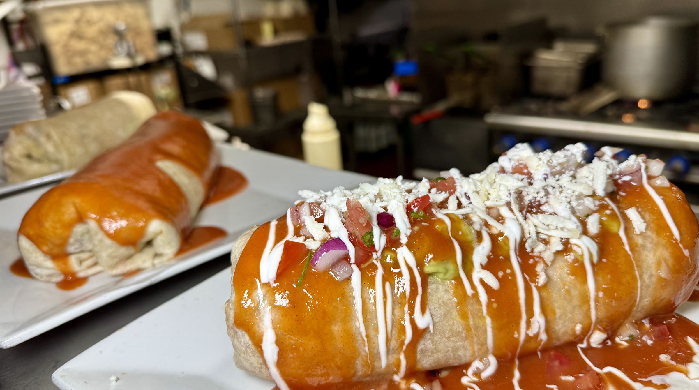 A Macho burrito covered in sauce, crema and cheese on a white plate in the Mi Pueblo kitchen in Santa Rosa